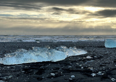 Shining sculptural ice on a black beach with ocean in background