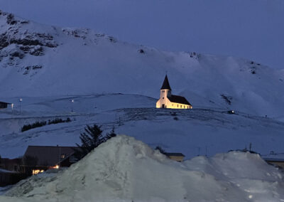 Nightfall casts a blue glow over Vik. A church is lit in yellow.