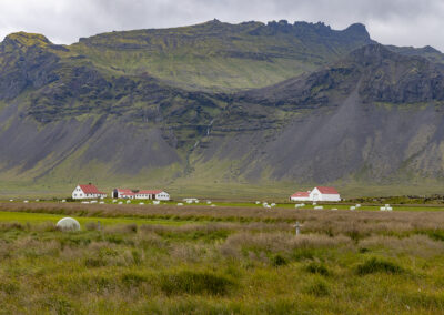 Mountains overlook a landscape with hay bales and farm buildings