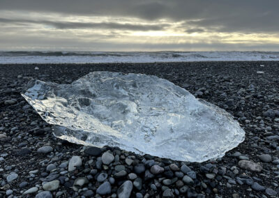 Sculptural ice on a black beach in Iceland with rays of sun coming through the clouds