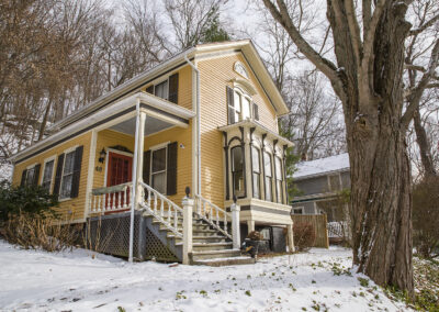 A yellow folk Victorian Italianate house with a red door