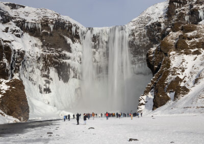 Icelandic waterfall with icicles and visitors in foreground