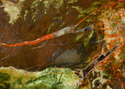 A red mineral intrusion resembles a chili pepper on a rust and green background