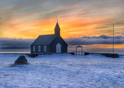 A black church in a snow field with a brilliant pastel sky