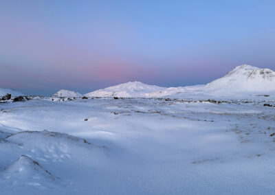 A snowy scene with hills and a pastel hued sky
