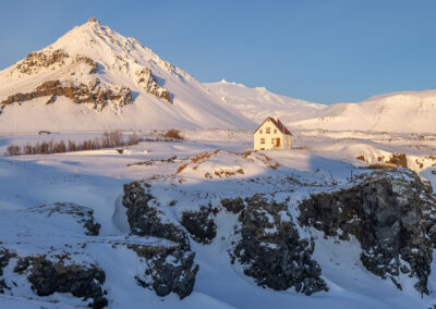 A snowy scene with a hill and lone house near Arnarstapi village