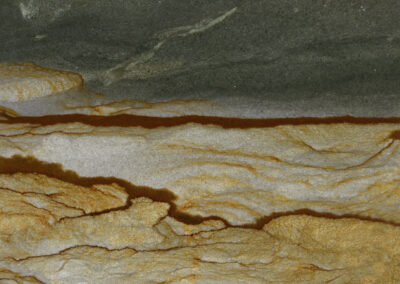 Mineral cross section of gray and tan with large rust-colored veins suggesting an aerial view of a river