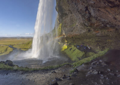 An Icelandic waterfall sprays a rainbowed mist into the river
