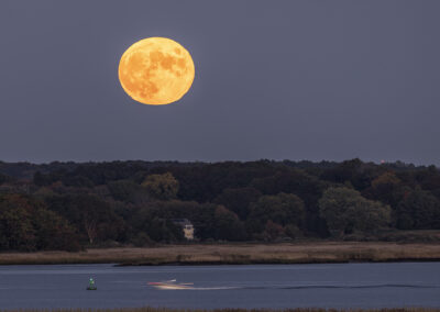 A large yellow moon over the Connecticut River with a boat going past
