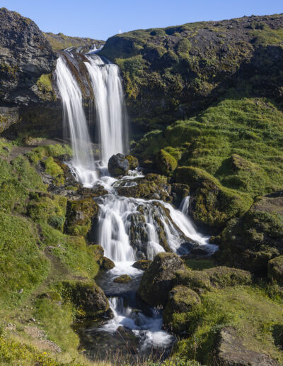 A waterfall in Iceland surrounded by green hills