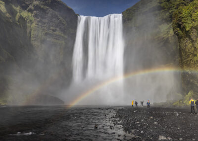 A rainbow arcs over visitors at Skogafoss waterfall