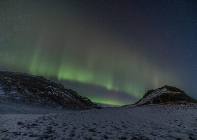 Northern lights cast a green glow over a snowy landscape