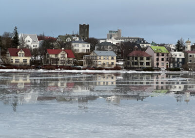 A row of detached houses lines a semi-frozen pond