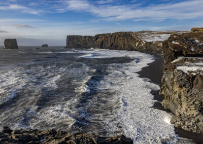 Rocky shoreline with waves crashing on black beach