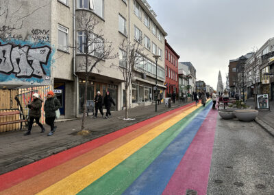A rainbow road leads down an Icelandic street with shops and a large spire at the end