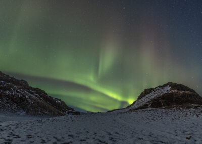 Northern lights cast a green glow over a snowy landscape