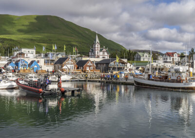 Húsavík harbor with boats, buildings and a traditional church with a green hill int he background